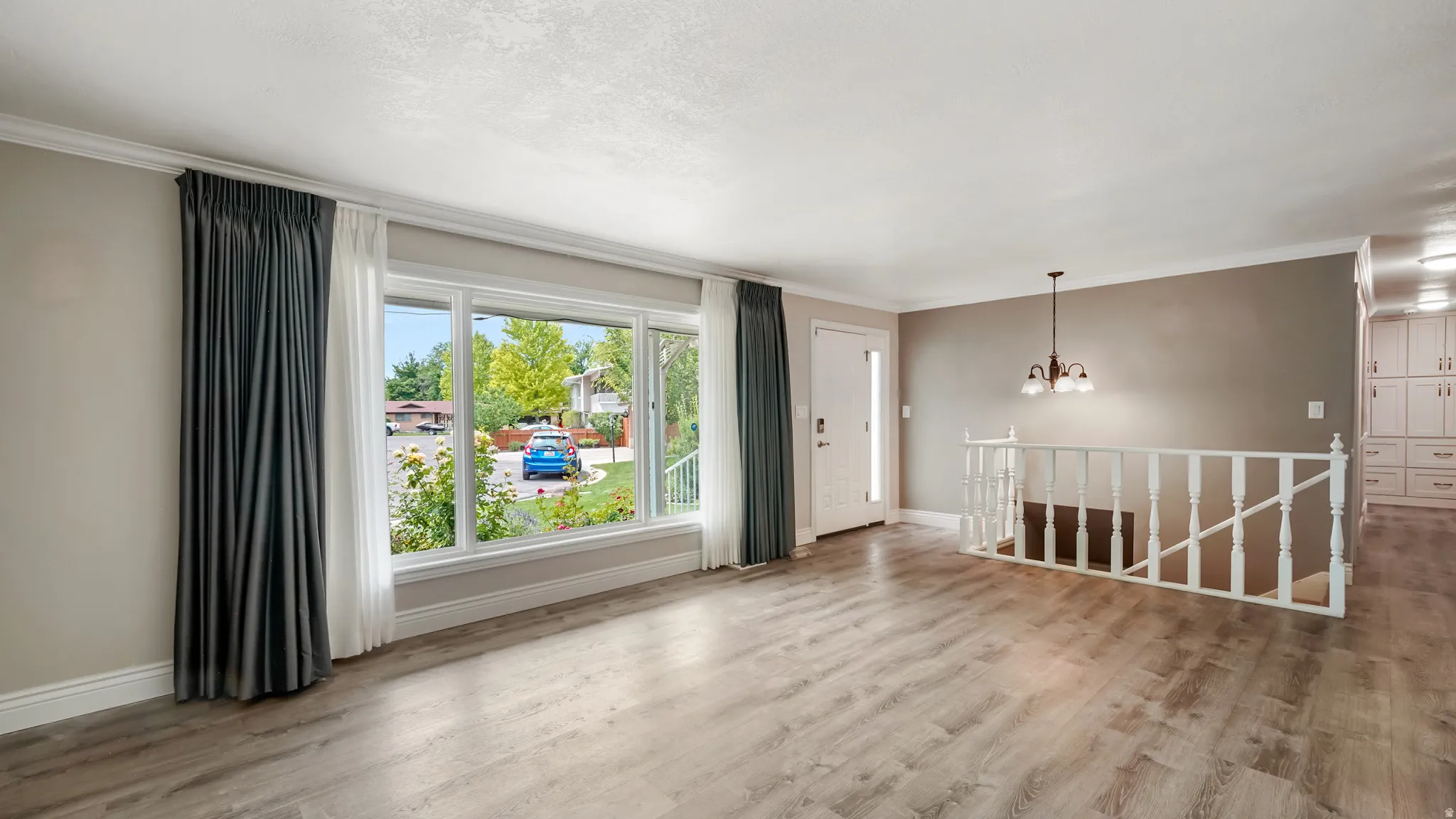 Spacious living area featuring wood-finish flooring, a large bay window, and a white spindle staircase