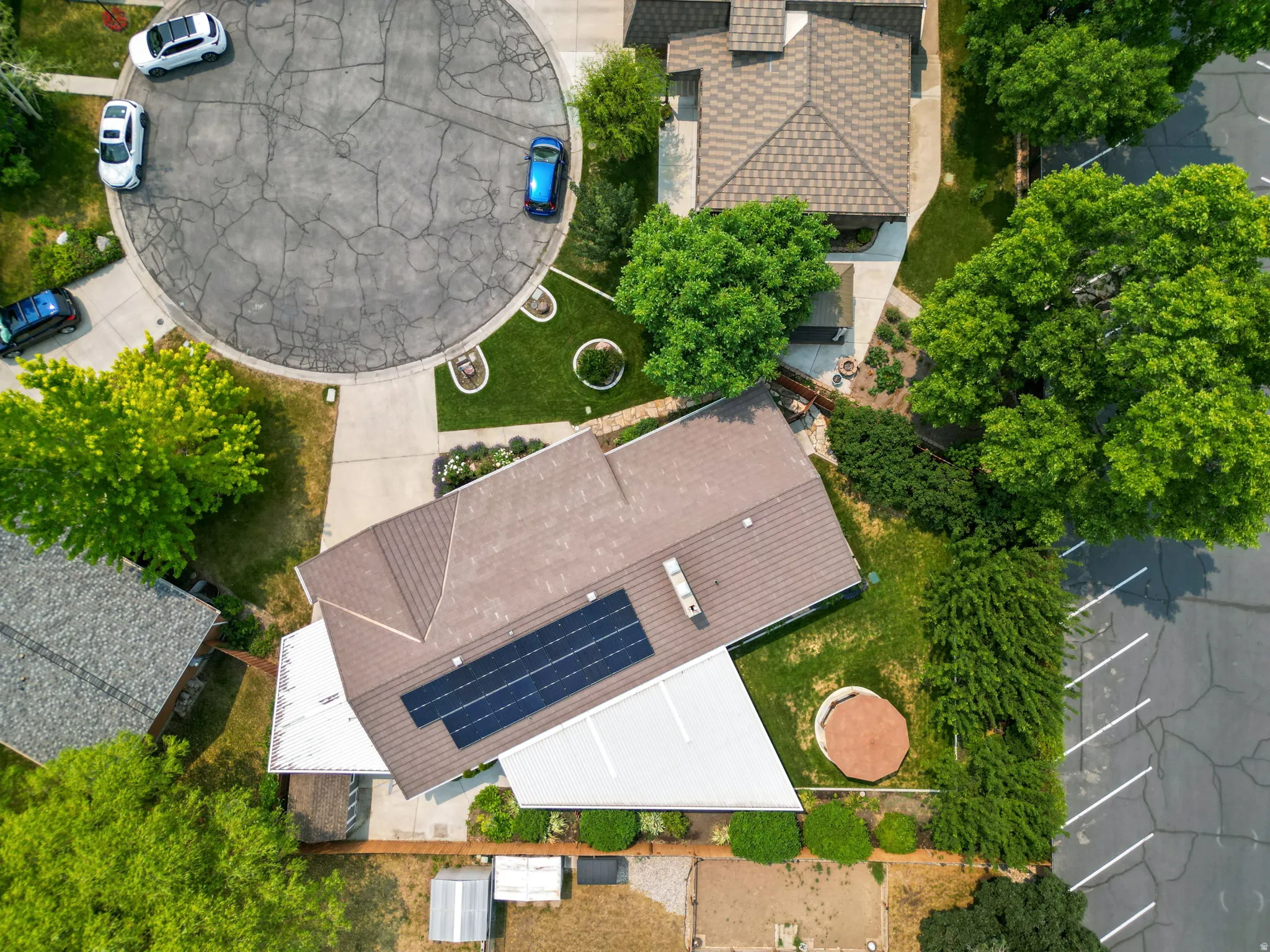 Residential property featuring a brown shingle roof, solar panel array, and mature landscaping