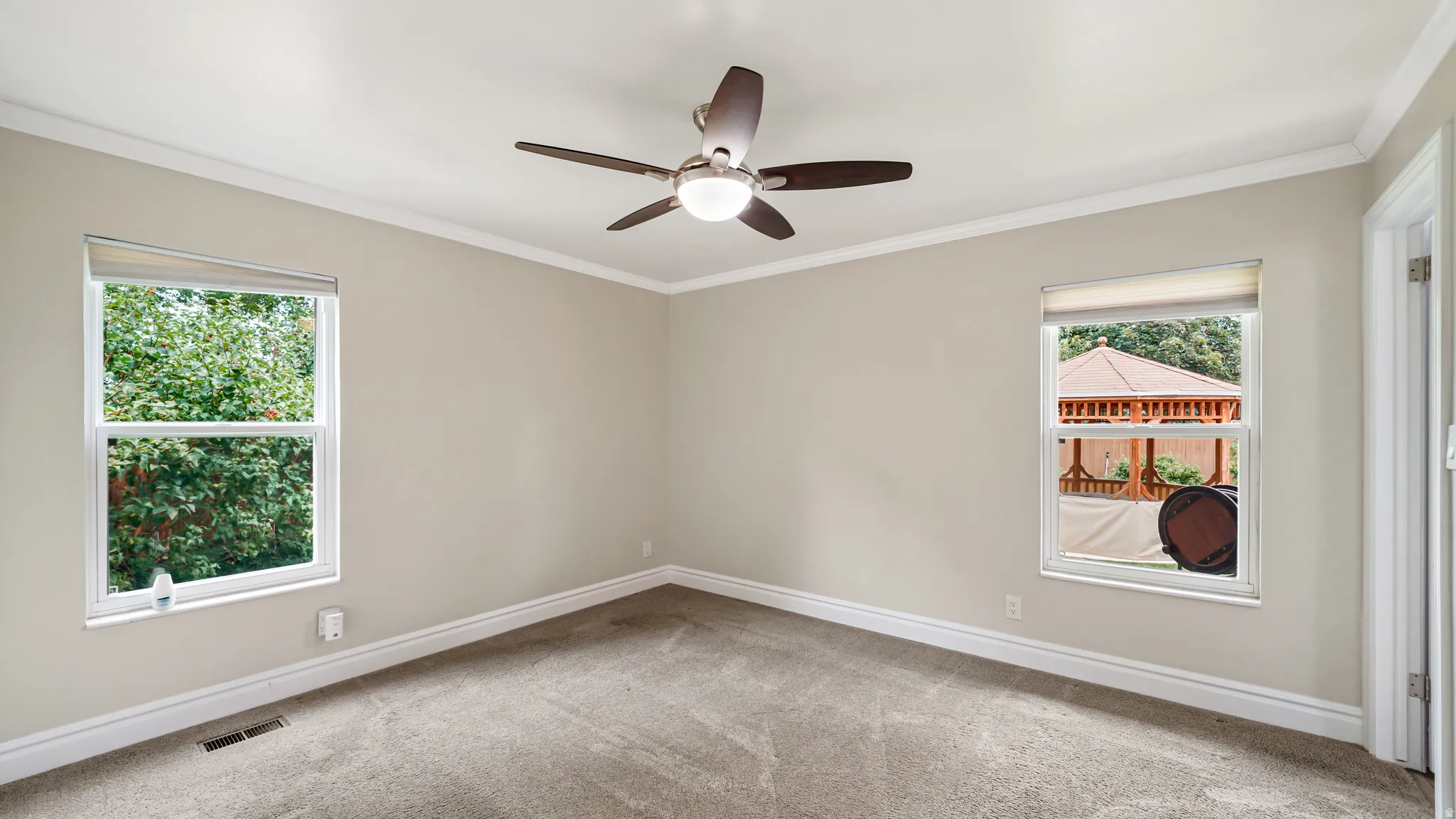 Carpeted room featuring a ceiling fan with integrated lighting, twin windows, crown molding, and baseboards