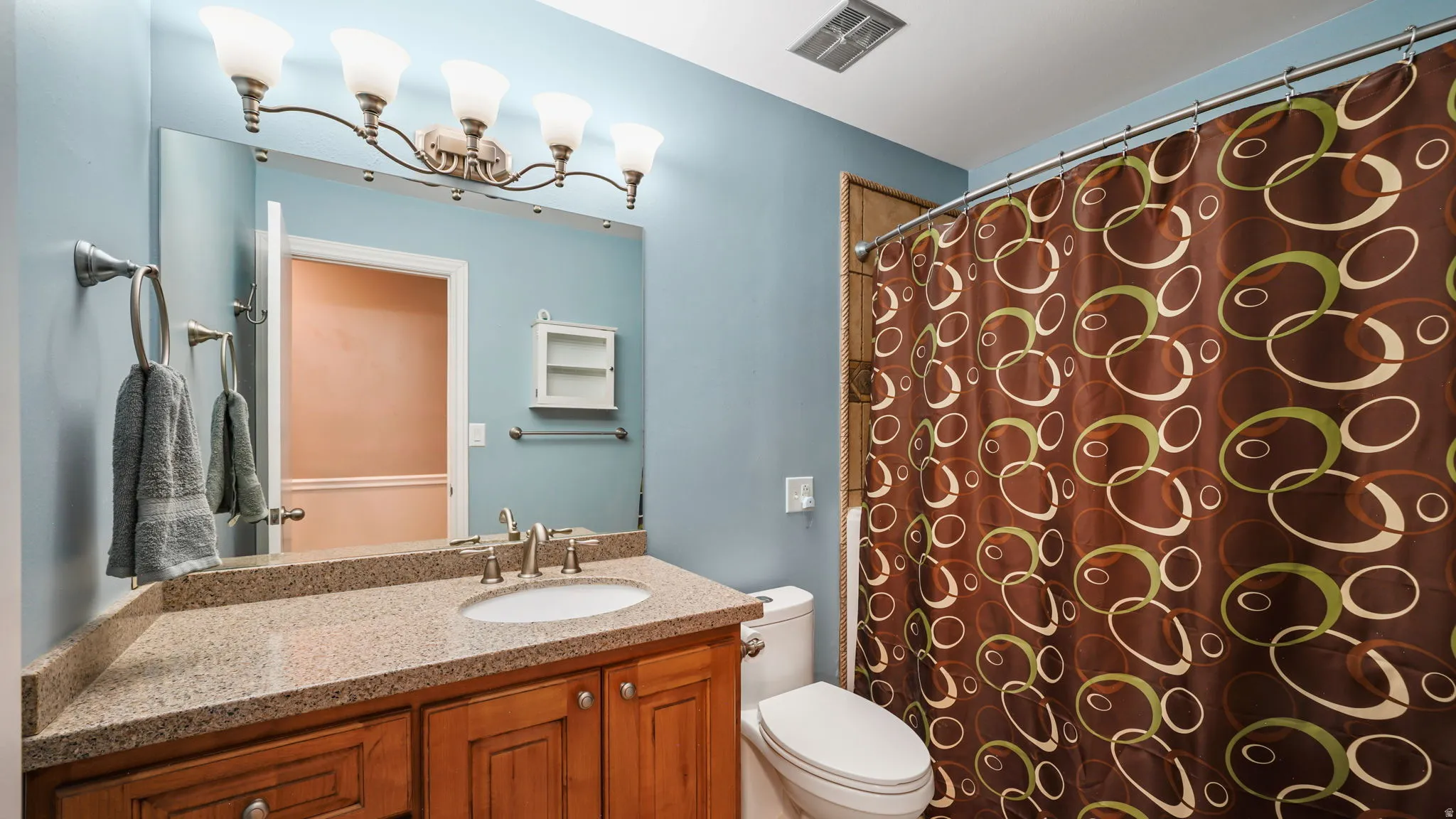Bathroom vanity with wood-finish cabinetry, a light-toned countertop, and an oval undermount sink