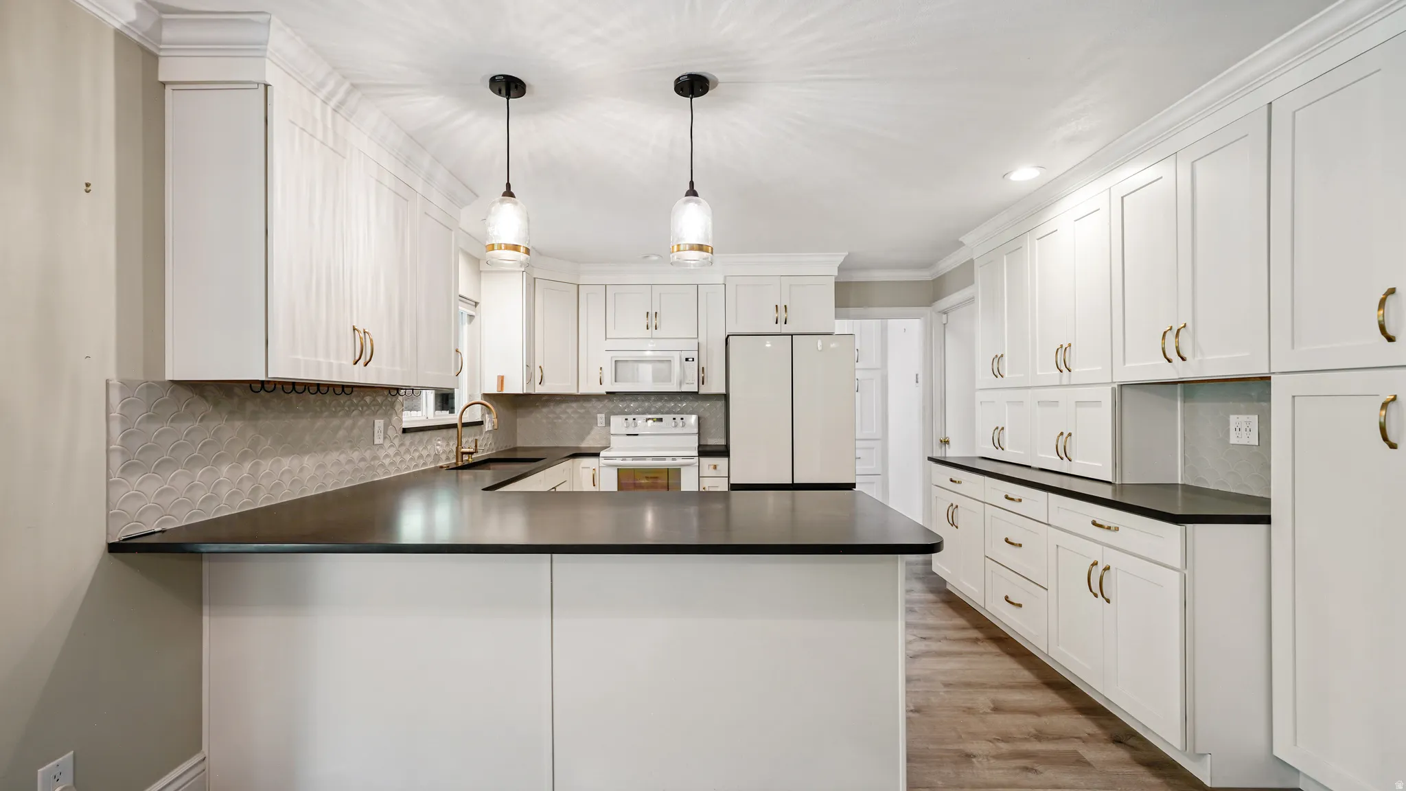 Modern kitchen featuring extensive white cabinetry, dark countertops, wood-finish flooring, and a decorative tile backsplash