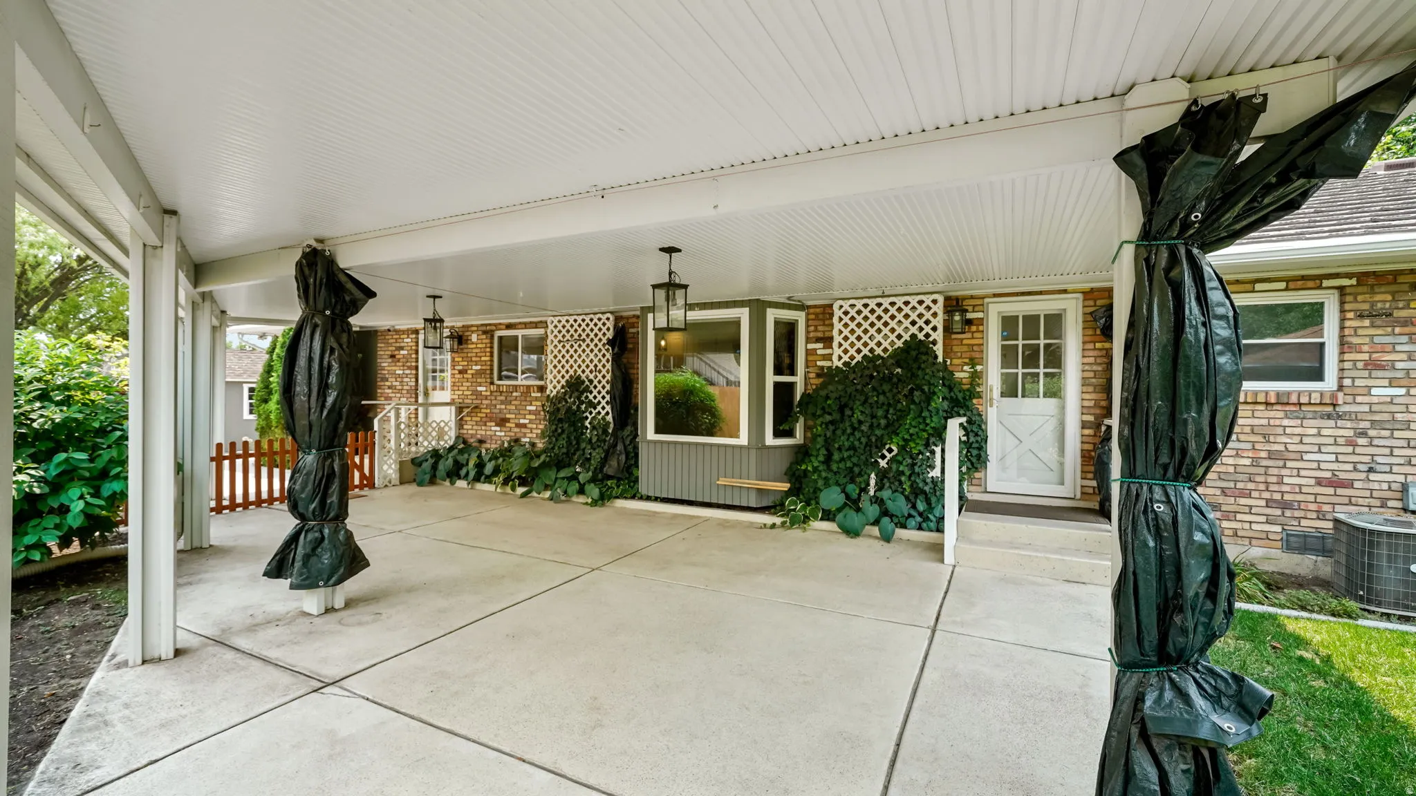 Expansive covered patio featuring a concrete surface, white lattice architectural accents, and exterior wall lanterns