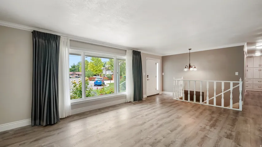 Spacious living area featuring wood-finish flooring, a large bay window, and a white spindle staircase
