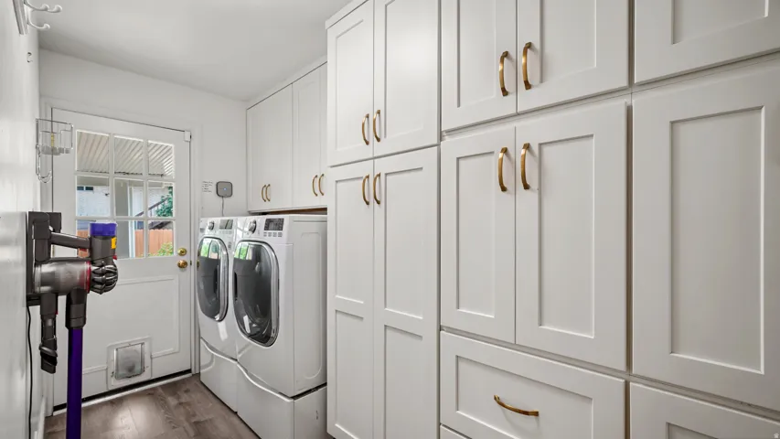 Laundry room featuring extensive white shaker cabinetry, gold-toned hardware, wood-finish flooring, and a glass-paneled door