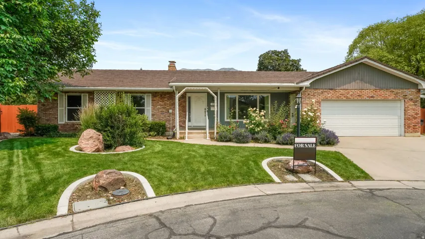 Brick exterior with an attached garage, featuring a concrete driveway and mature landscaping with decorative boulders
