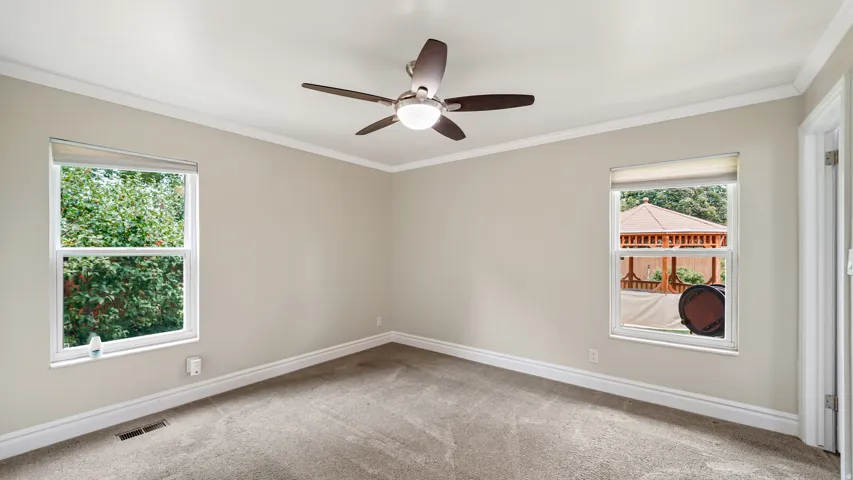 Carpeted room featuring a ceiling fan with integrated lighting, twin windows, crown molding, and baseboards