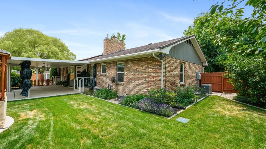 Expansive backyard featuring a manicured lawn, a covered patio, brick exterior, mature trees, and a privacy fence