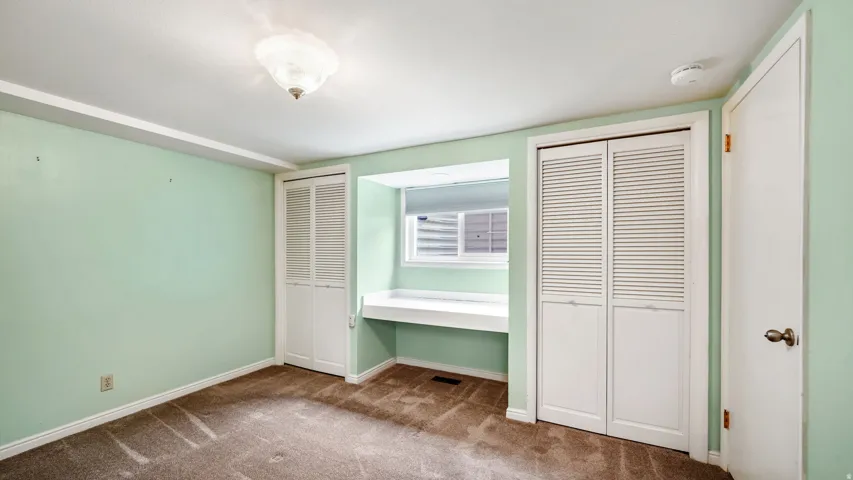 Room featuring a built-in window desk, two sets of louvered bi-fold closet doors, wall-to-wall carpeting, and a flush-mount ceiling light fixture