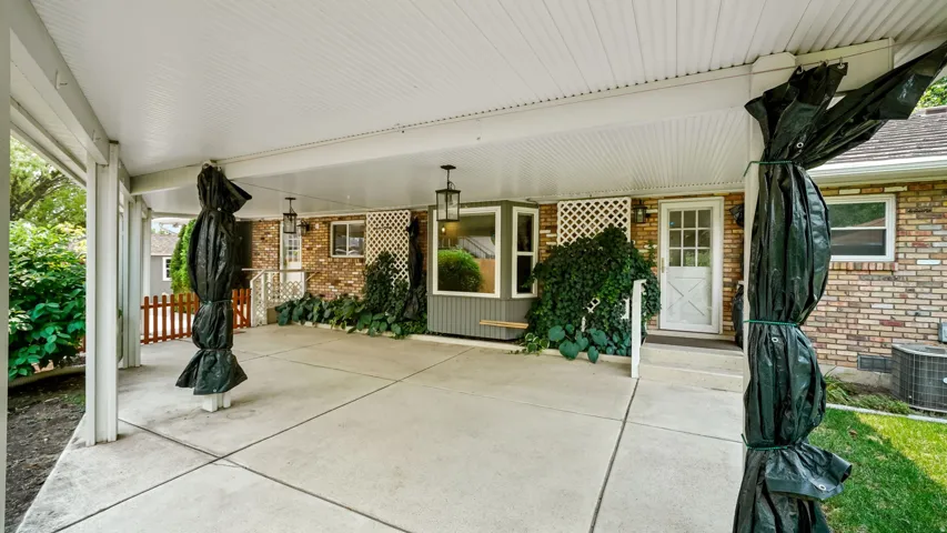 Expansive covered patio featuring a concrete surface, white lattice architectural accents, and exterior wall lanterns
