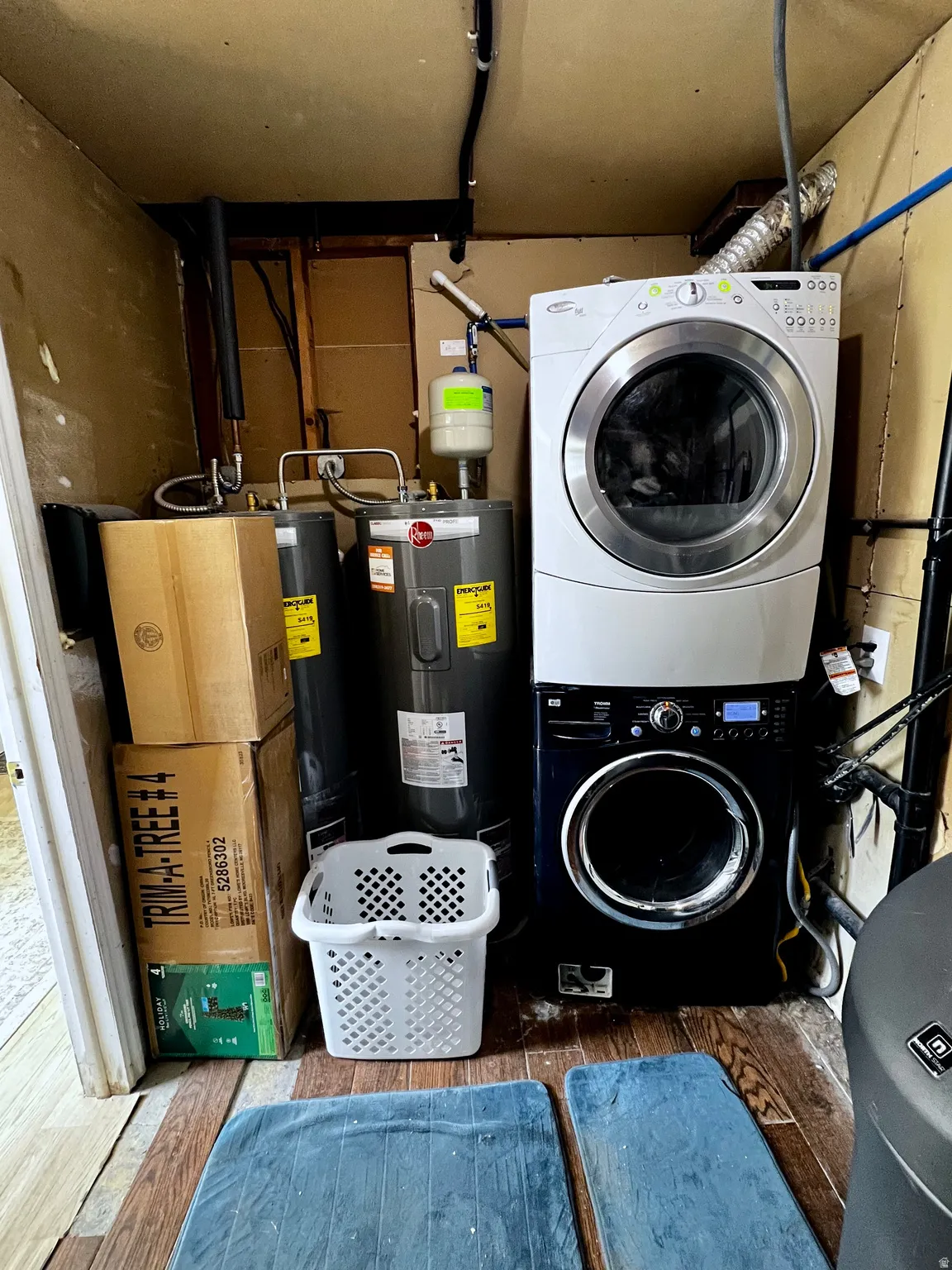 Utility area featuring wood-finish flooring, two large water heaters, and a stacked washer and dryer