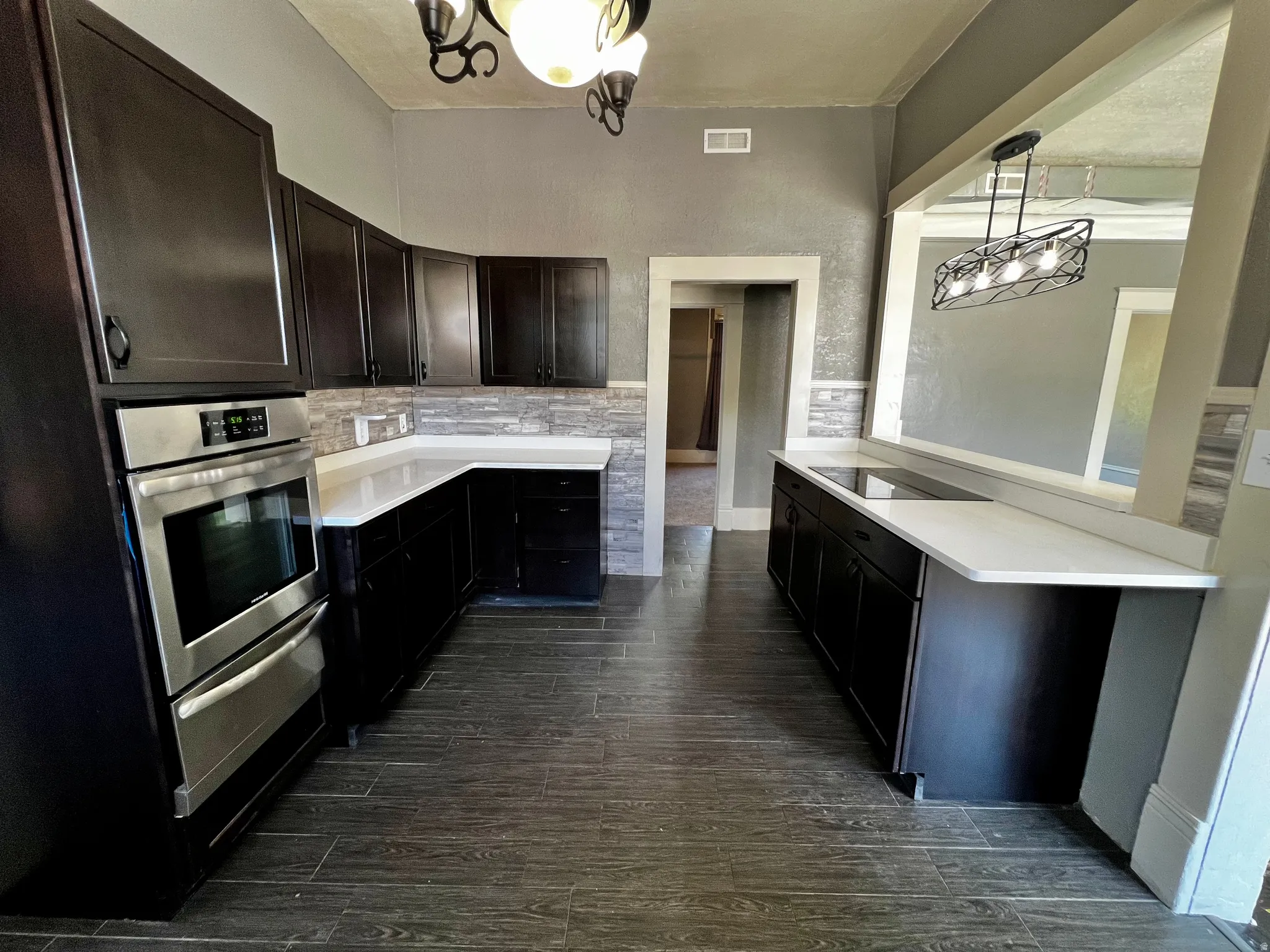 Kitchen featuring dark wood-finish cabinetry, white solid surface countertops, stacked stone backsplash, and wood-look tile flooring