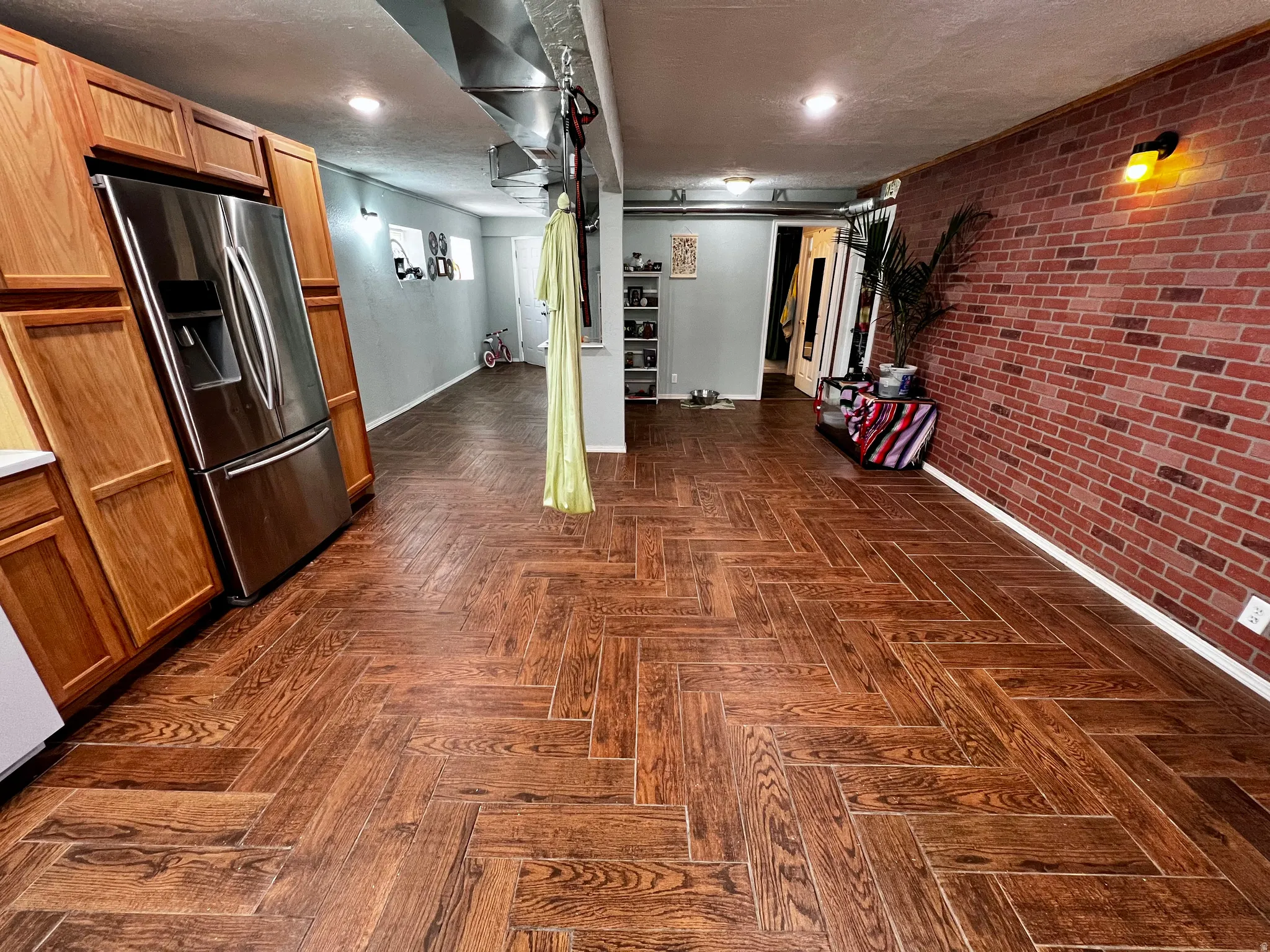 Expansive room featuring wood-finish flooring with a herringbone pattern, exposed brick accent wall, and recessed lighting