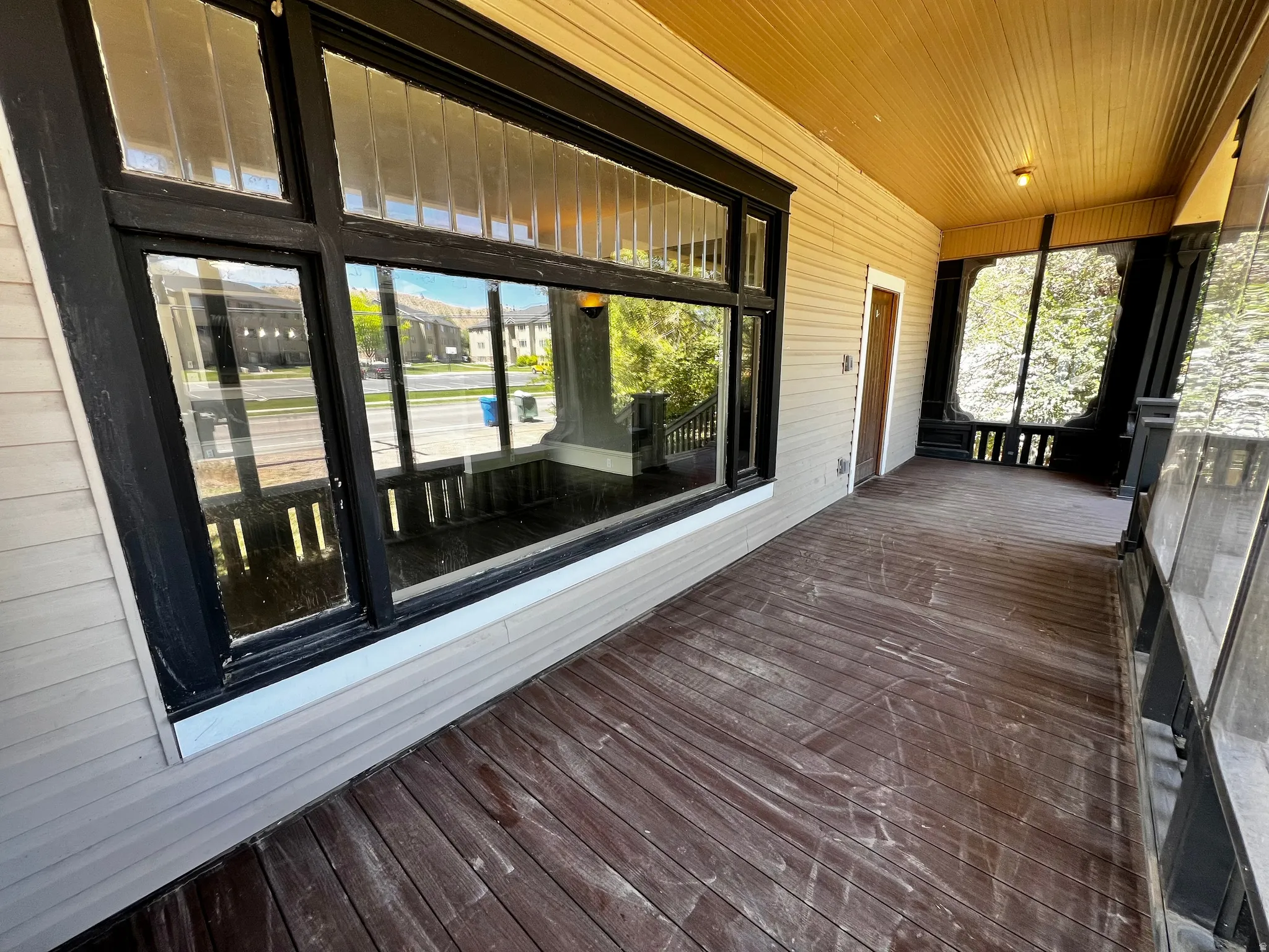 Expansive front porch featuring wood-finish flooring, light-colored siding, and a contrasting dark window frame