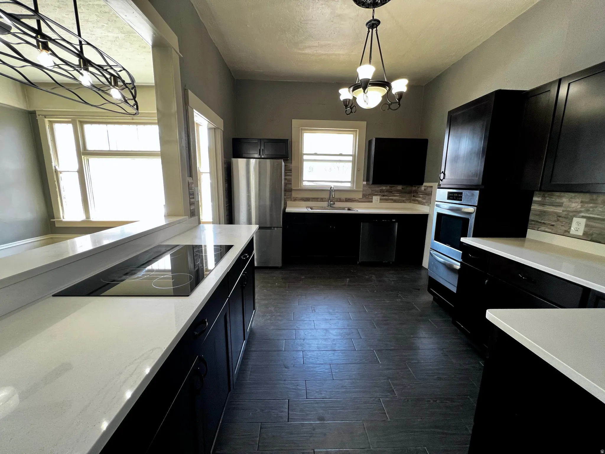 Modern kitchen featuring dark cabinetry, light countertops, integrated cooktop, stainless steel appliances, and a tiled backsplash