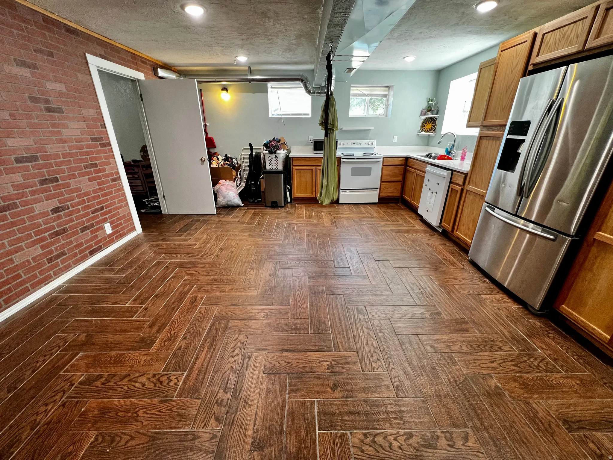 Herringbone wood-finish flooring extending into a kitchen area with light wood cabinetry and a stainless steel refrigerator