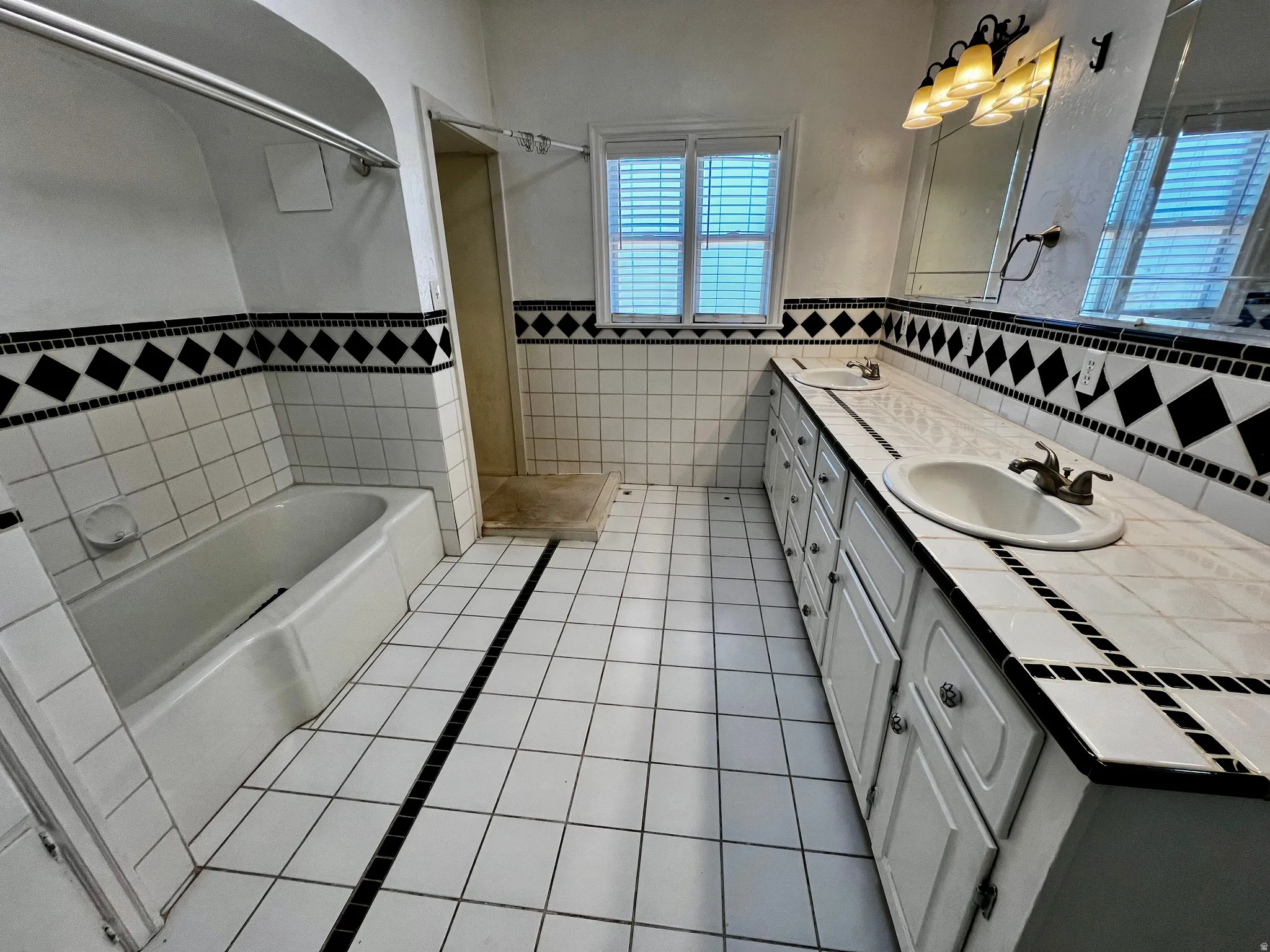 Bathroom featuring a dual vanity with tile countertop, integrated sinks, and under-cabinet storage