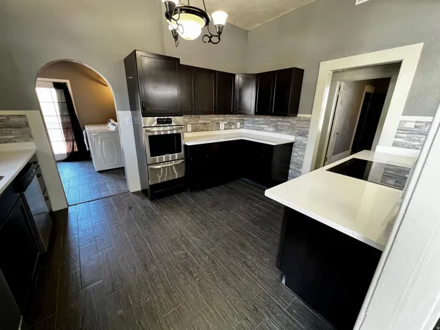 Kitchen featuring dark wood-finish flooring, black cabinetry, light countertops, a built-in stainless steel oven, and a built-in cooktop