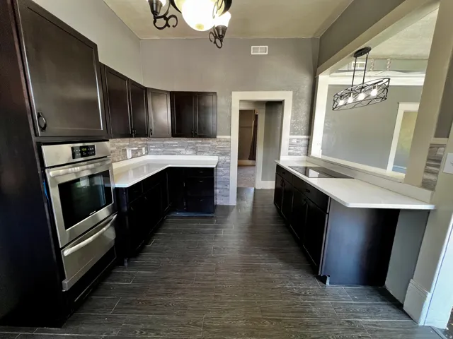 Kitchen featuring dark wood-finish cabinetry, white solid surface countertops, stacked stone backsplash, and wood-look tile flooring