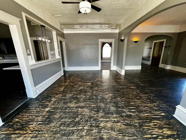 Spacious interior featuring distinctive wood-finish flooring, a contemporary ceiling fan with light, and arched doorways