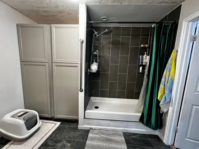 Spacious shower with dark tiled surround and white shower pan
