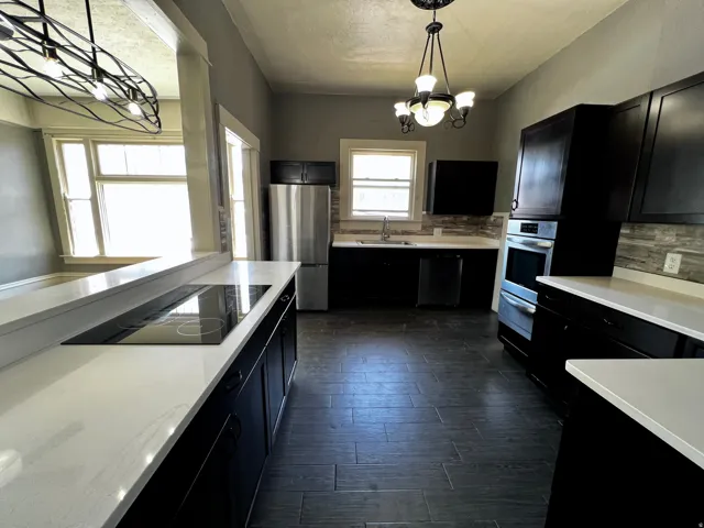 Modern kitchen featuring dark cabinetry, light countertops, integrated cooktop, stainless steel appliances, and a tiled backsplash