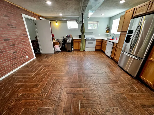 Herringbone wood-finish flooring extending into a kitchen area with light wood cabinetry and a stainless steel refrigerator