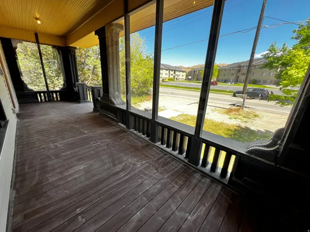 Screened-in porch featuring dark wood plank flooring, a slatted balustrade, and substantial decorative columns