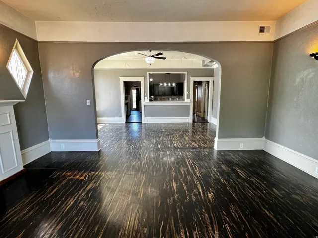 Expansive living area featuring rich, dark wood-finish flooring, a diamond-pane window, and an arched doorway leading to additional interior spaces