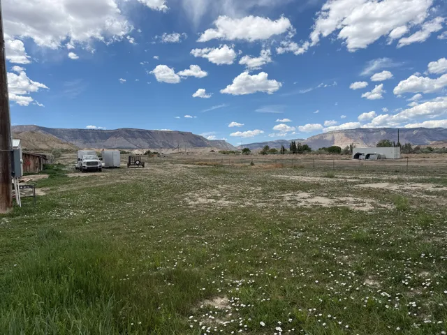Expansive open field with natural ground cover, featuring distant mountains and a blue sky with scattered clouds