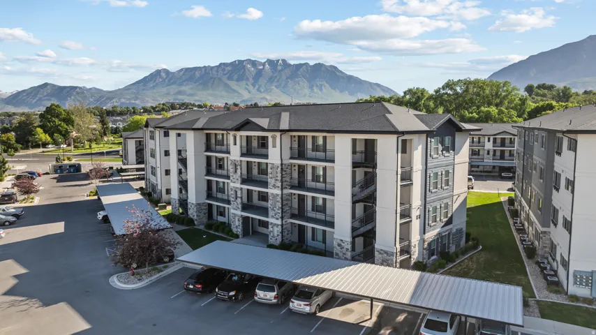 Modern apartment building featuring a multi-tone facade with stone accents, individual balconies, dark-pitched roofs, and covered parking structures