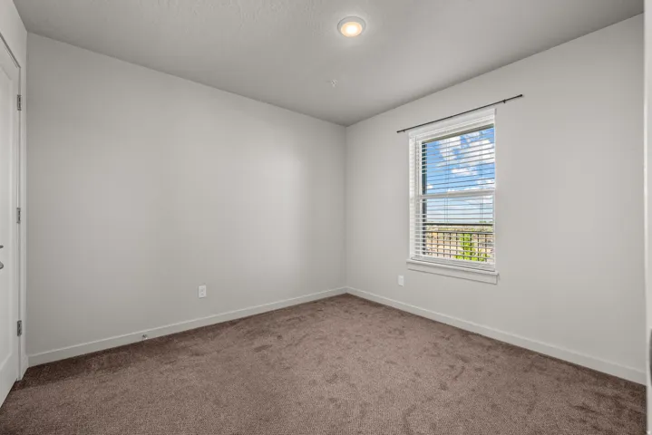 Neutral-toned room featuring a single window with blinds, recessed ceiling lighting, textured carpet, and a white interior door