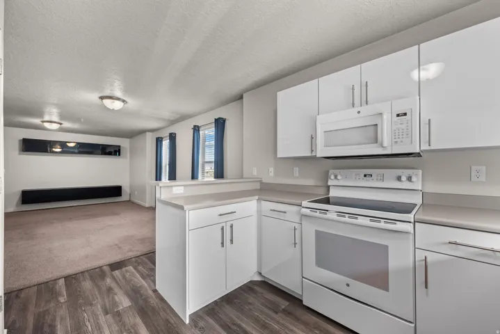 Modern kitchen featuring white cabinetry, light countertops, wood-finish flooring, and white appliances