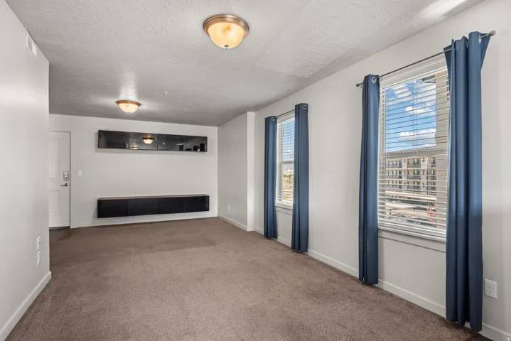 Carpeted room featuring two windows with horizontal blinds, a white door, and two flush-mount ceiling lights