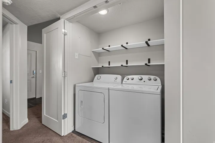 Dedicated laundry closet featuring a washer and dryer, complemented by two levels of built-in shelving with black support brackets