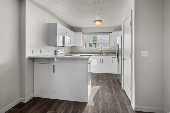 Kitchen featuring white cabinetry, light-toned countertops, a stainless steel sink, and wood-finish flooring