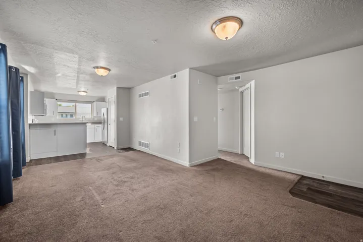 Open-concept living area featuring neutral-toned carpet, light gray walls, and two flush-mount ceiling lights