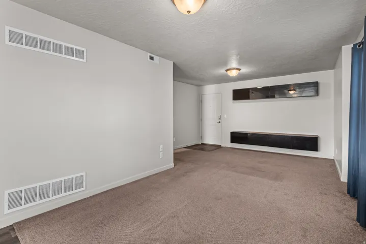 Spacious living area featuring neutral carpeting, a white entry door, and overhead dome lighting fixtures