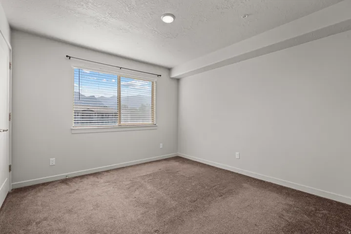 Carpeted room featuring light gray walls, a window with horizontal blinds, and a distant mountain scenery