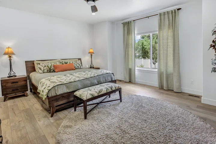 Bedroom featuring light LVP flooring, a contemporary ceiling fan, and a large window with drapes