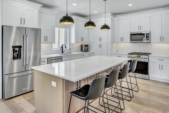 Kitchen featuring a large island with seating, stainless steel appliances, white shaker cabinetry, pendant lighting, and LVP flooring