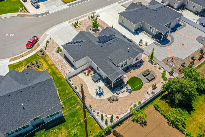 Expansive backyard featuring a covered patio, artificial turf area, two raised garden beds, and decorative gravel landscaping with mature shrubs