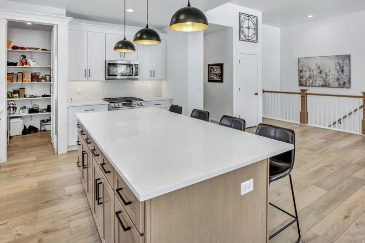 Modern kitchen featuring a large central island with quartz countertop, white cabinetry, a subway tile backsplash, stainless steel appliances, and LVP flooring