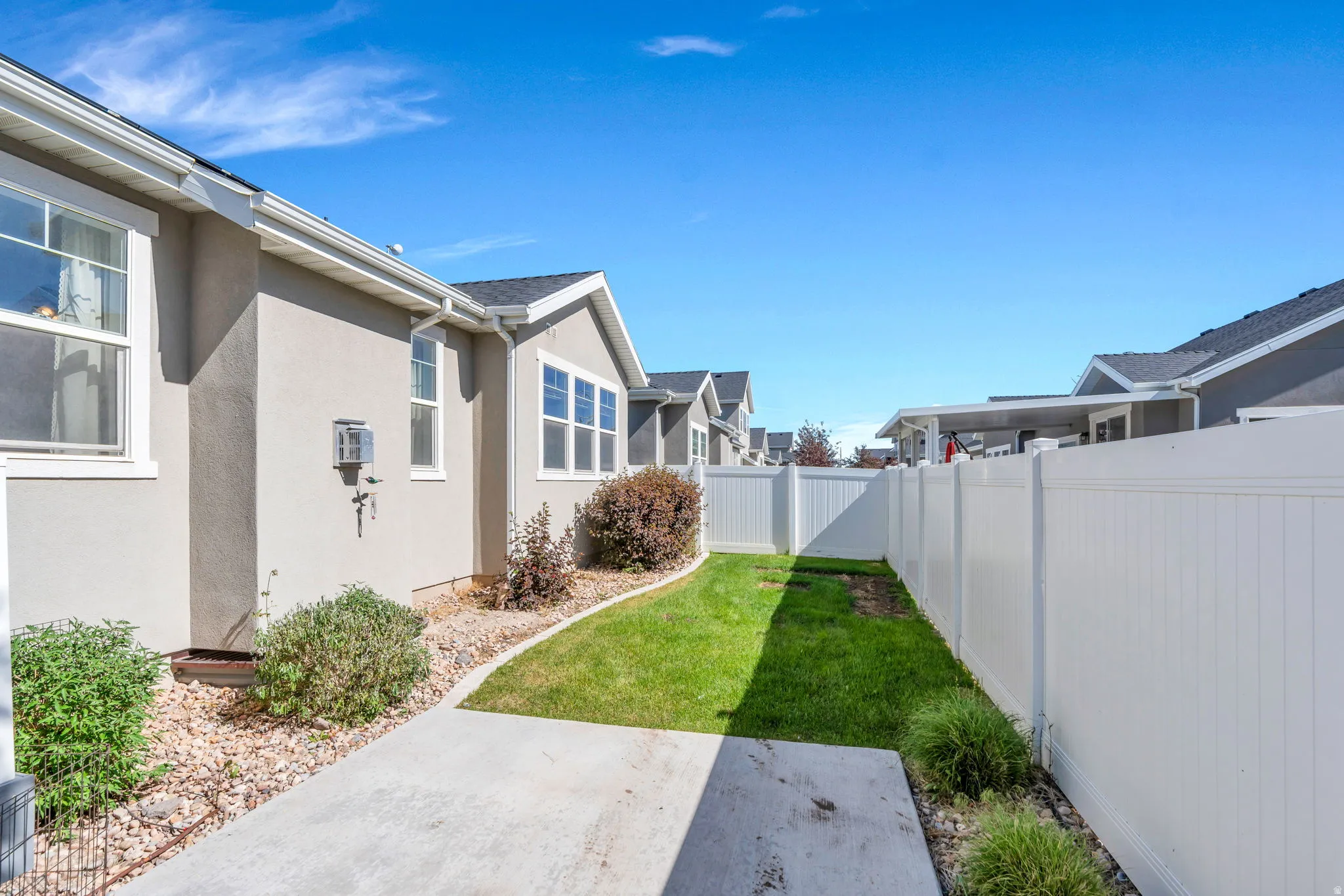 Landscaped side yard featuring a concrete path, a manicured lawn strip, and a white privacy fence