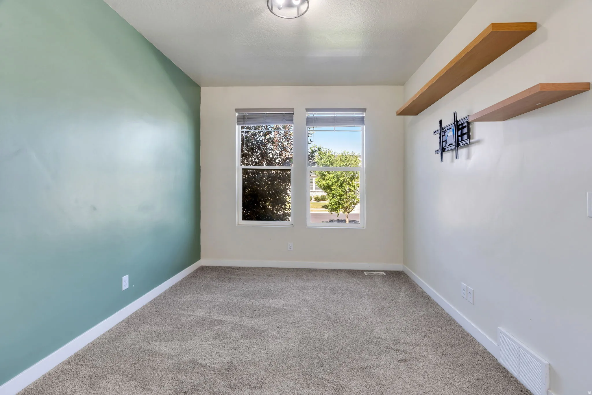 Carpeted room featuring a teal accent wall and two windows