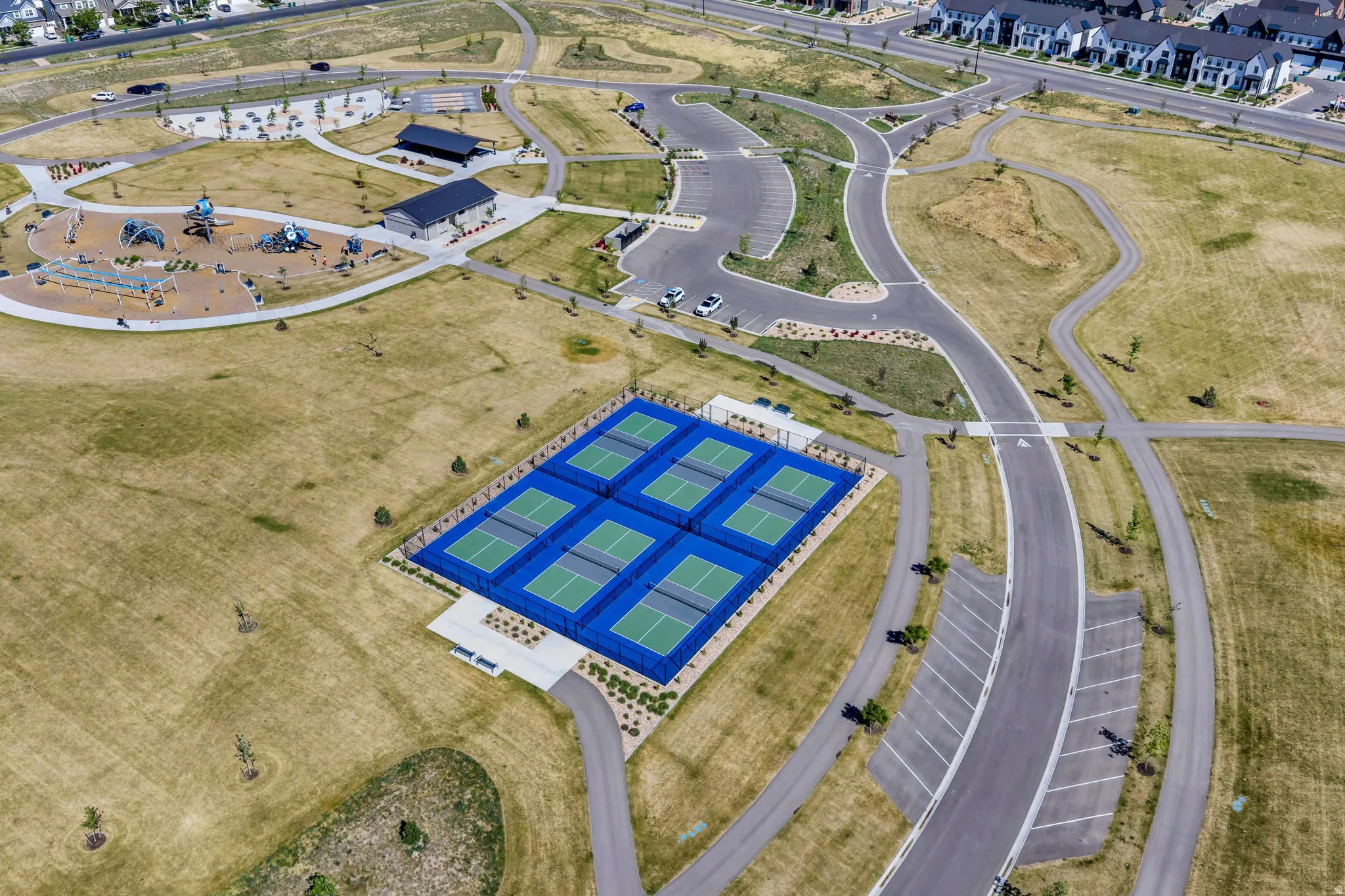 Recreational area featuring multiple blue and green sports courts, a playground with various structures, and a pavilion