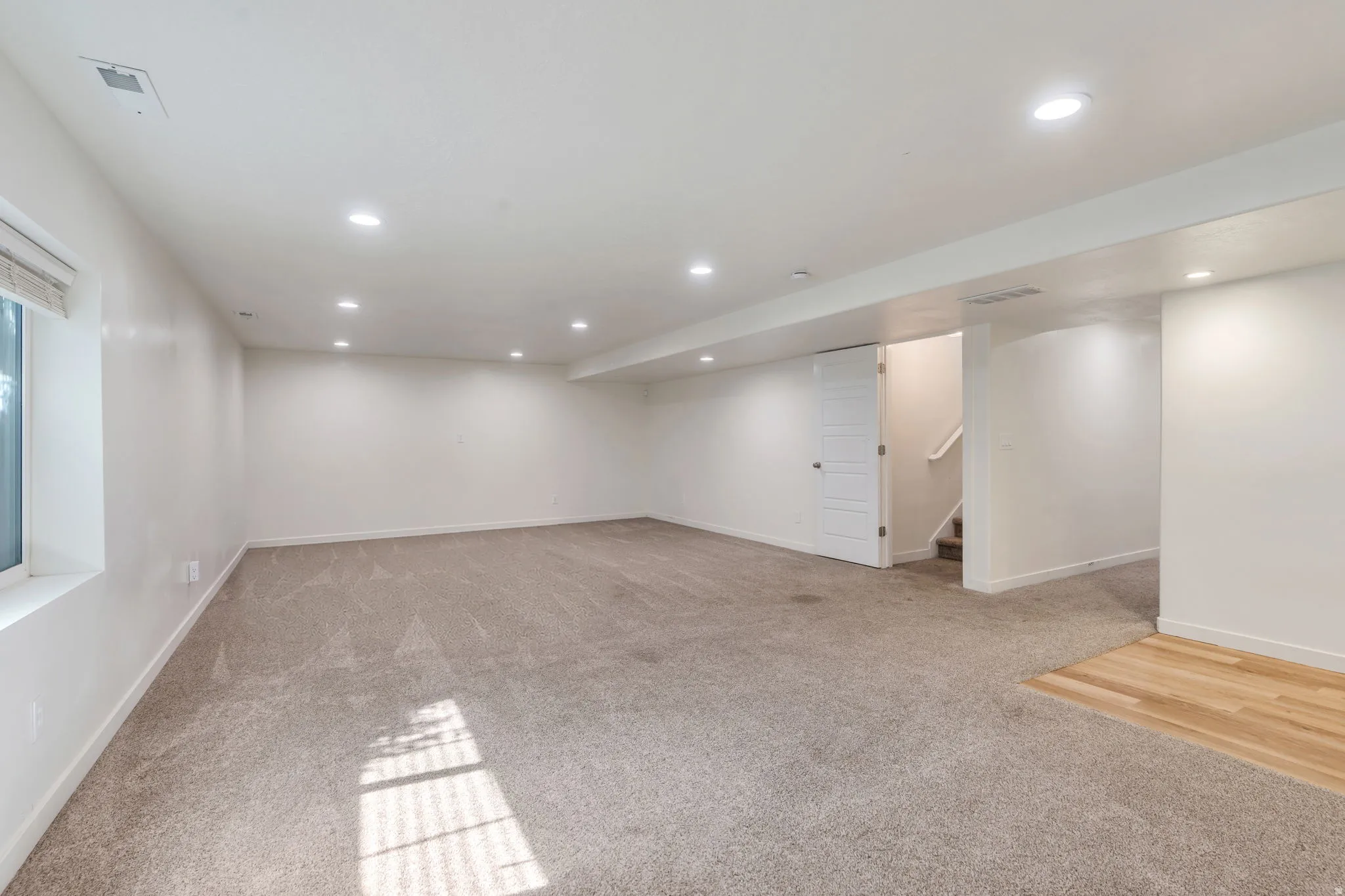 Spacious finished room featuring neutral carpet, recessed lighting, and a window with blinds