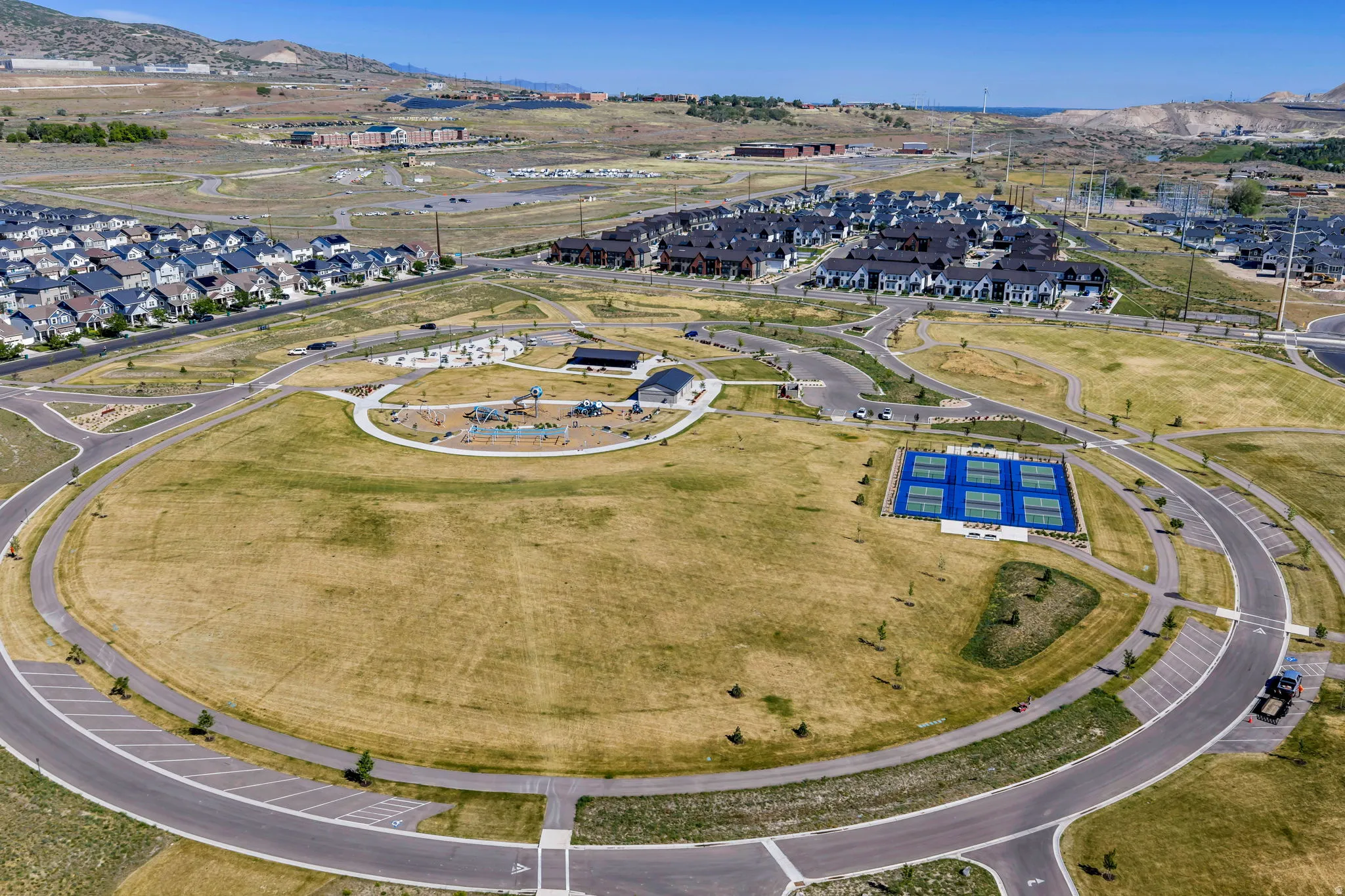 Expansive community park featuring a large grassy area, multiple tennis courts, and a dedicated playground