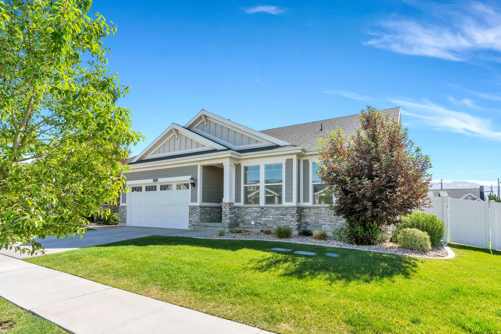 Ranch-style residence featuring a gray siding facade, stone accent details, a two-car garage, and a covered front porch