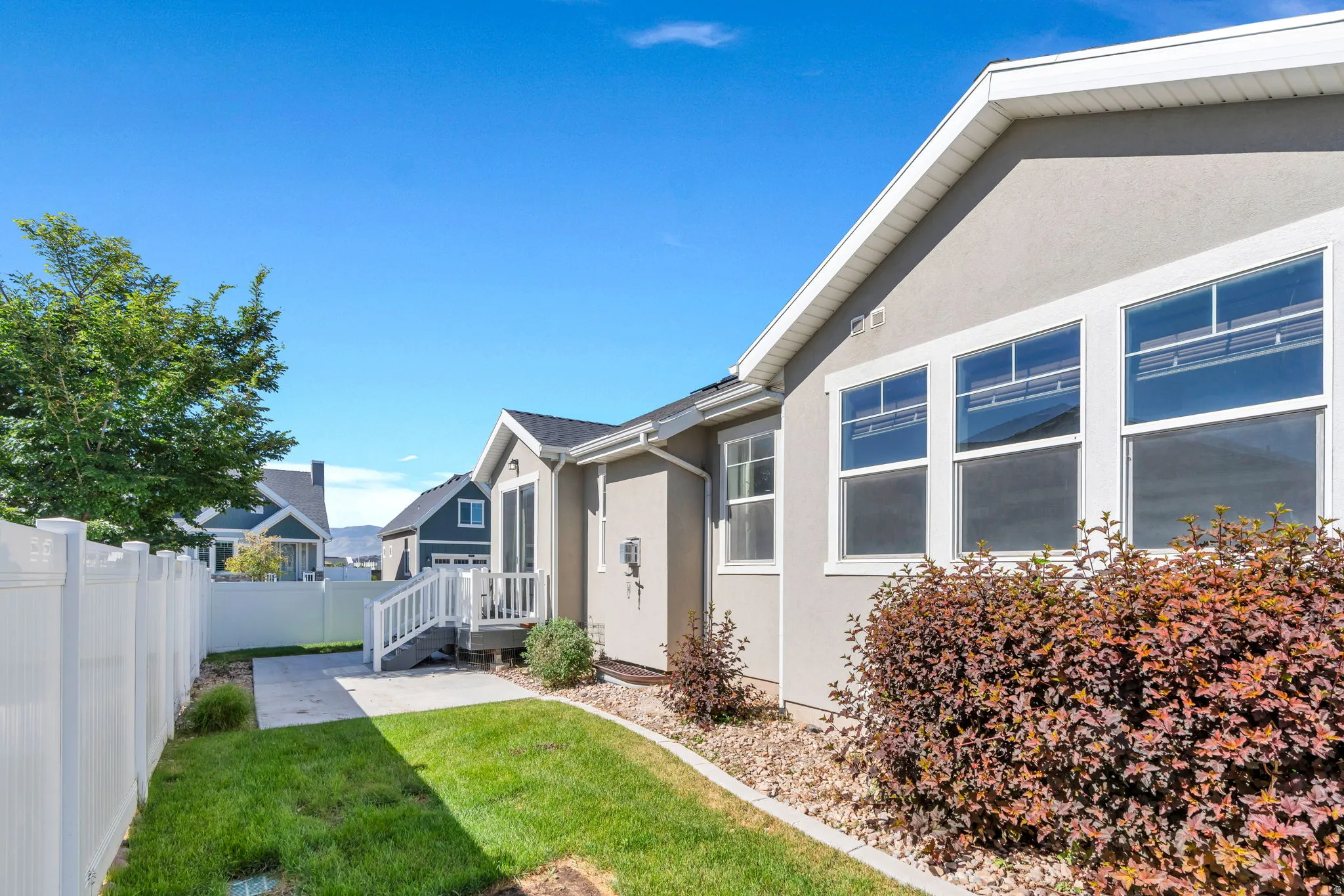 Exterior of the property featuring a stucco finish, multiple windows with white trim, a white vinyl fence, and a green lawn
