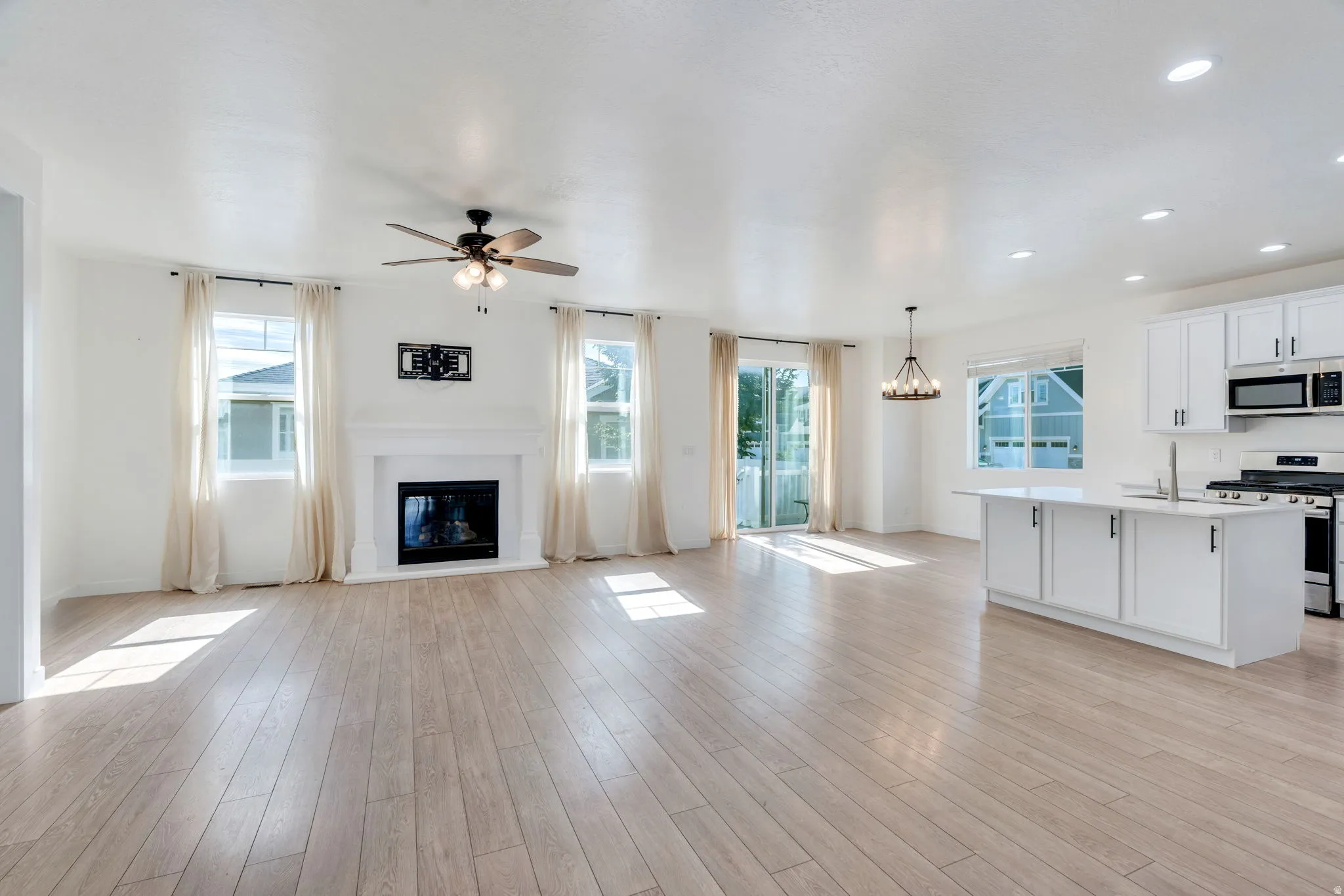 Open-concept living space with light wood-finish flooring, a white mantel fireplace, and a ceiling fan